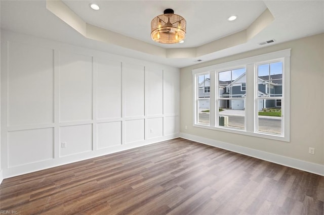 unfurnished room featuring dark wood-type flooring, a tray ceiling, visible vents, and a decorative wall