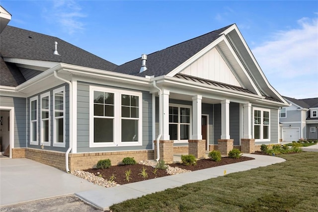 view of front of property with metal roof, covered porch, brick siding, a shingled roof, and a standing seam roof