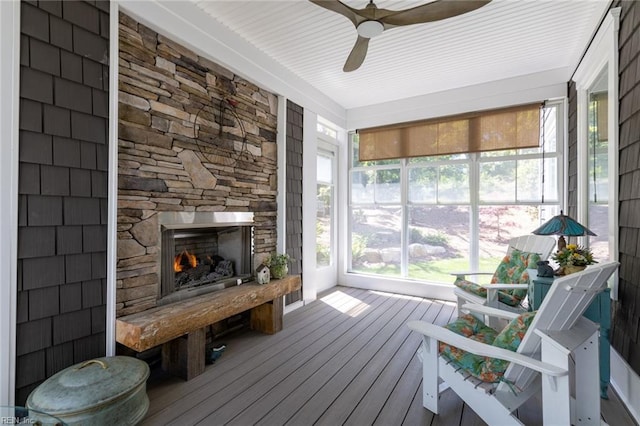 sunroom with a ceiling fan, a wealth of natural light, and a stone fireplace