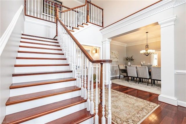 stairway with ornate columns, hardwood / wood-style floors, a chandelier, and ornamental molding