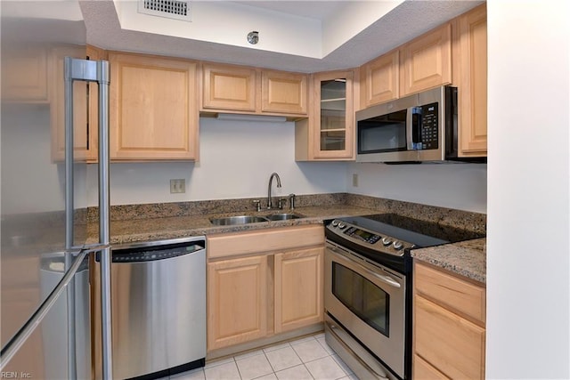 kitchen featuring appliances with stainless steel finishes, sink, light brown cabinets, light tile patterned floors, and dark stone countertops