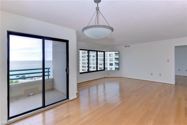 empty room featuring a textured ceiling, light hardwood / wood-style floors, and a water view