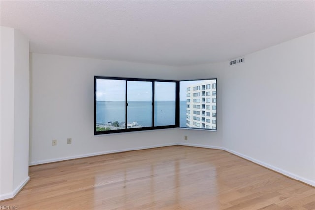 unfurnished room with light hardwood / wood-style floors and a water view