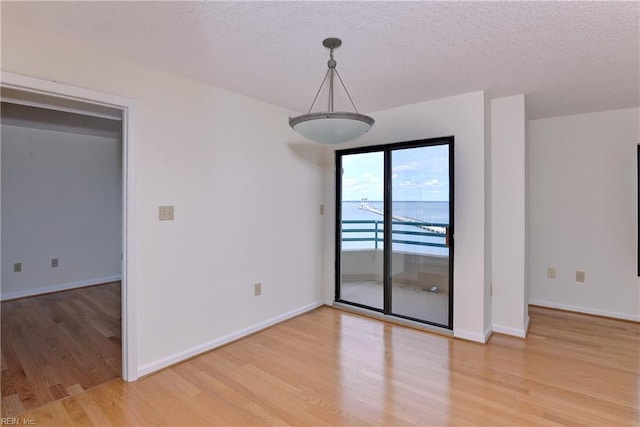 spare room featuring a textured ceiling, light hardwood / wood-style floors, and a water view