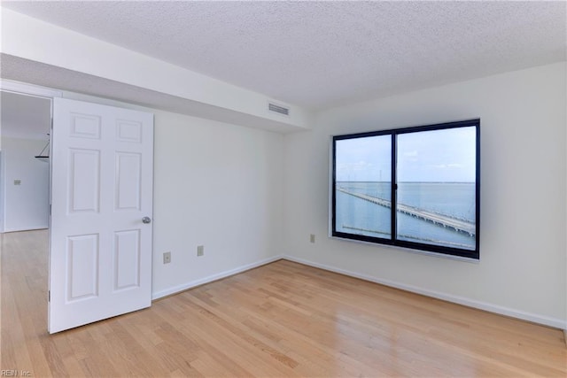 unfurnished room with a textured ceiling, light hardwood / wood-style flooring, and a water view