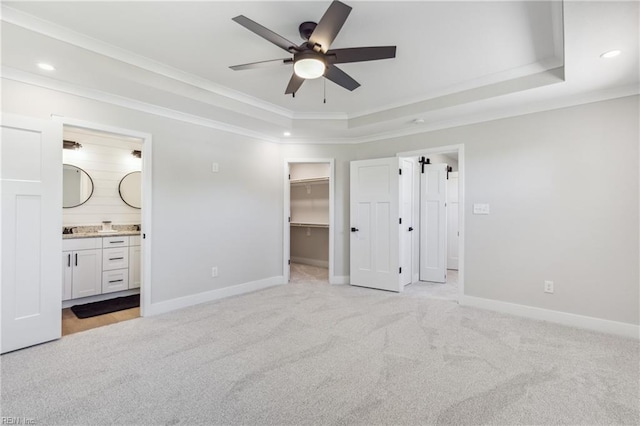 unfurnished bedroom featuring a walk in closet, ensuite bathroom, light colored carpet, a raised ceiling, and ceiling fan