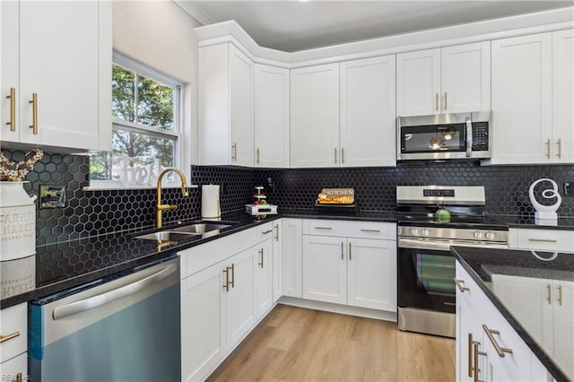 kitchen featuring white cabinetry, sink, backsplash, appliances with stainless steel finishes, and light wood-type flooring