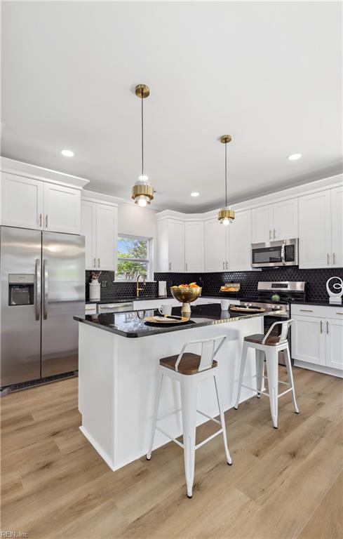 kitchen featuring tasteful backsplash, light hardwood / wood-style flooring, pendant lighting, and appliances with stainless steel finishes