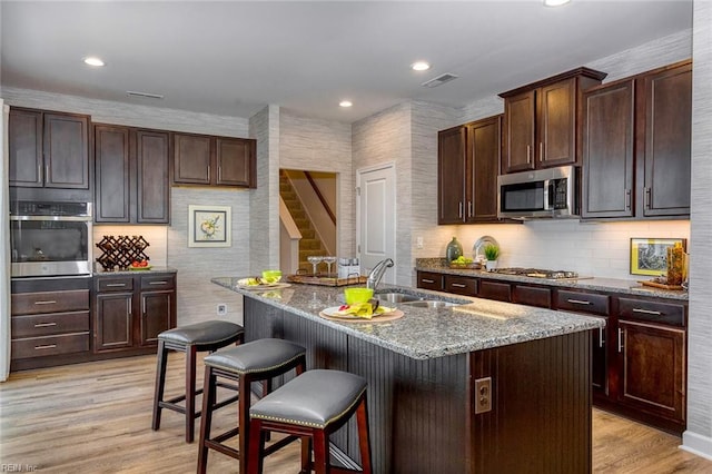 kitchen featuring appliances with stainless steel finishes, a kitchen island with sink, dark stone countertops, and light wood-type flooring