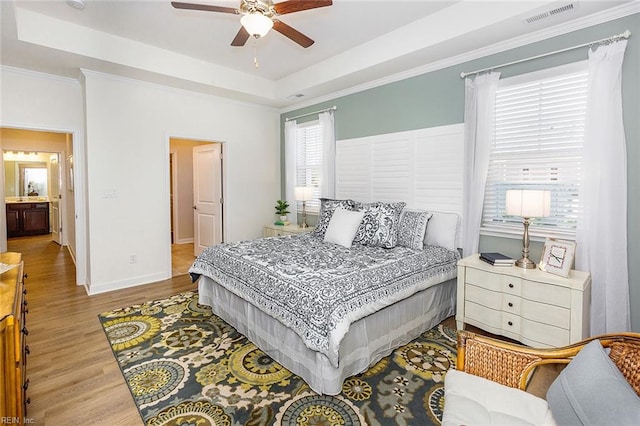 bedroom featuring a tray ceiling, ceiling fan, light wood-type flooring, and ensuite bathroom