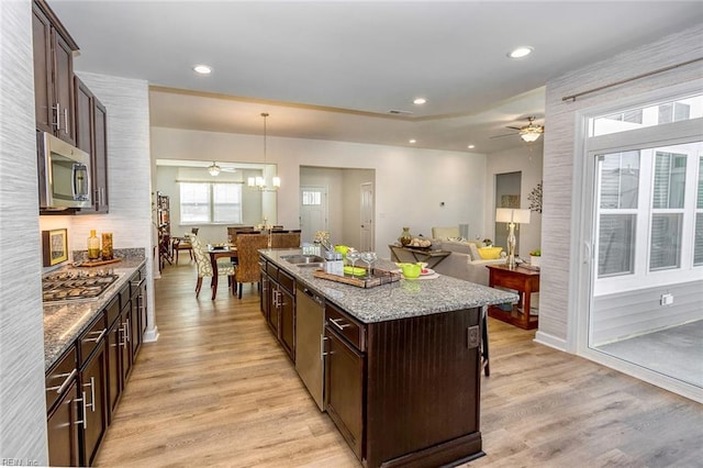 kitchen with decorative light fixtures, appliances with stainless steel finishes, light stone countertops, light hardwood / wood-style floors, and ceiling fan