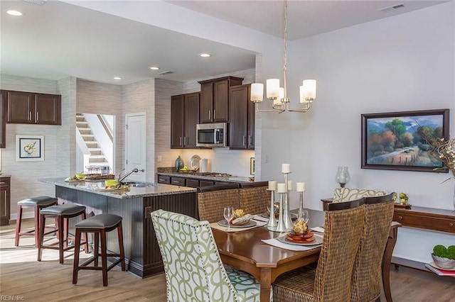 kitchen featuring hanging light fixtures, light hardwood / wood-style flooring, appliances with stainless steel finishes, and dark brown cabinets