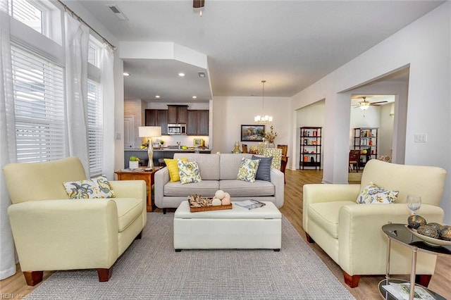 living room with ceiling fan with notable chandelier and hardwood / wood-style flooring