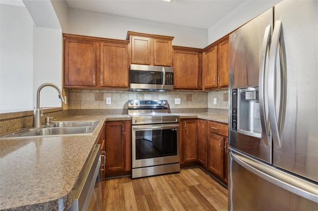 kitchen featuring sink, backsplash, appliances with stainless steel finishes, and light hardwood / wood-style flooring