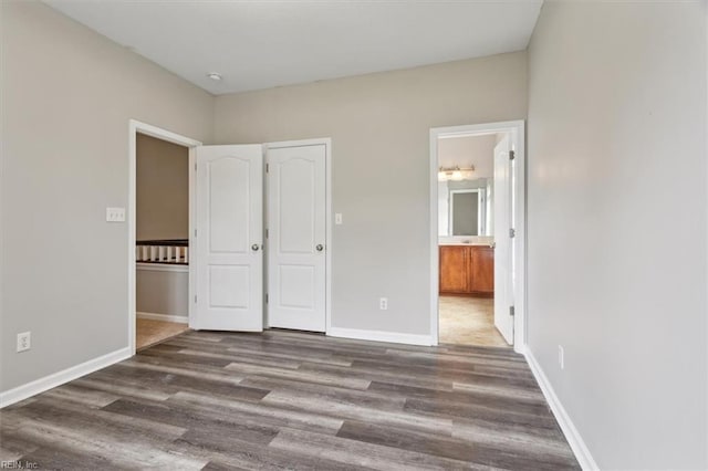 unfurnished bedroom with ensuite bath and wood-type flooring