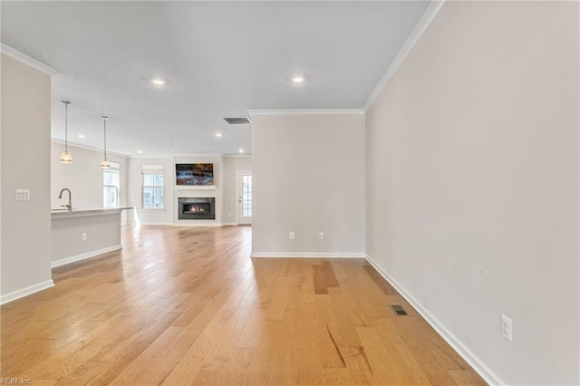 unfurnished living room featuring sink, crown molding, and light hardwood / wood-style flooring