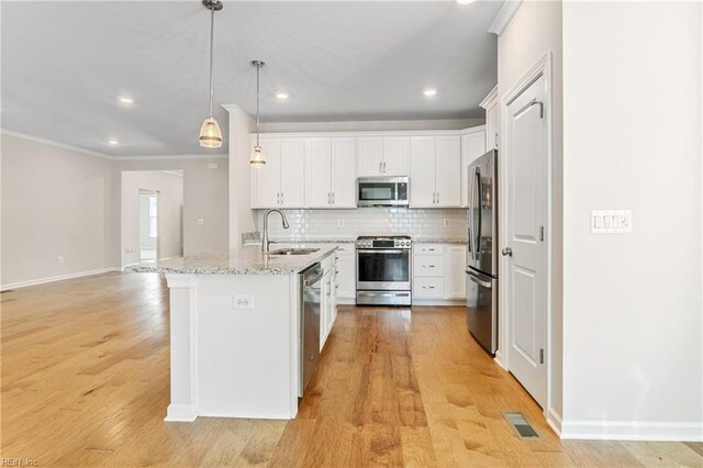 kitchen featuring appliances with stainless steel finishes, sink, white cabinets, a kitchen island with sink, and light stone countertops