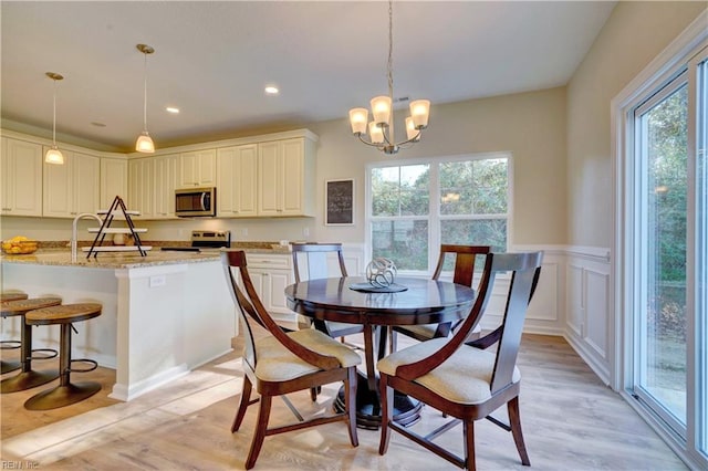 dining room featuring a chandelier, light wood-type flooring, recessed lighting, wainscoting, and a decorative wall