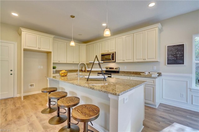 kitchen featuring pendant lighting, a sink, light stone counters, light wood-style floors, and appliances with stainless steel finishes