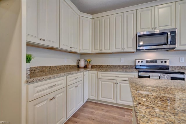 kitchen with stainless steel appliances, light stone countertops, white cabinets, and light wood finished floors