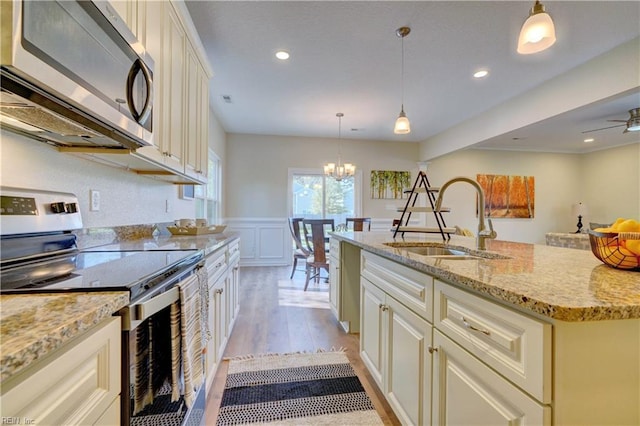 kitchen with light stone countertops, light wood-type flooring, an inviting chandelier, stainless steel appliances, and a sink