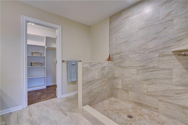 full bath featuring a spacious closet, tiled shower, and baseboards