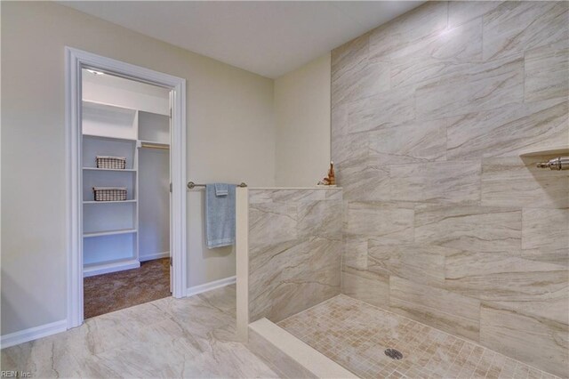 bathroom with a tile shower, a walk in closet, and baseboards