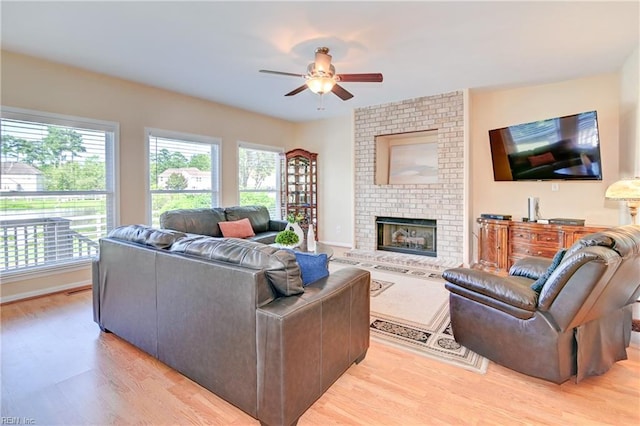 living room with ceiling fan, brick wall, light hardwood / wood-style floors, and a brick fireplace