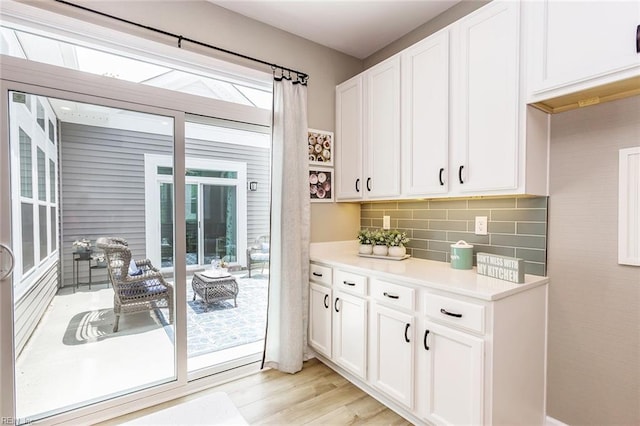 interior space with decorative backsplash, a healthy amount of sunlight, light wood-type flooring, and white cabinetry