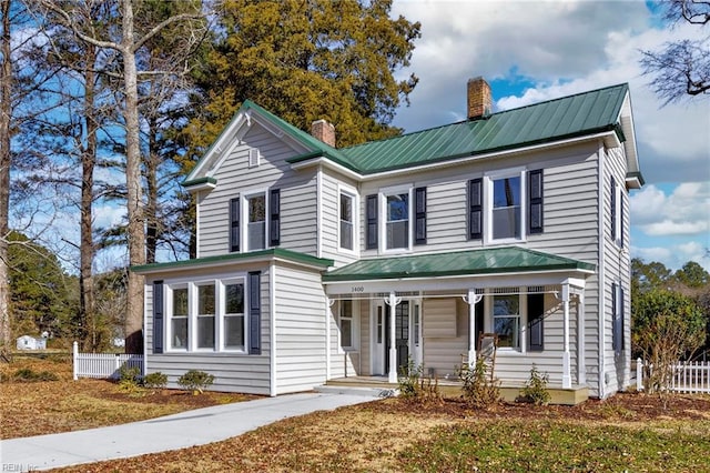 traditional home featuring metal roof, a porch, a chimney, and fence