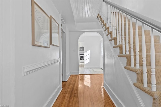 hall with arched walkways, hardwood / wood-style floors, stairway, and baseboards