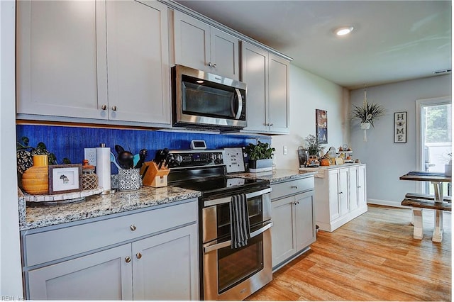 kitchen featuring light wood-type flooring, appliances with stainless steel finishes, light stone countertops, and tasteful backsplash