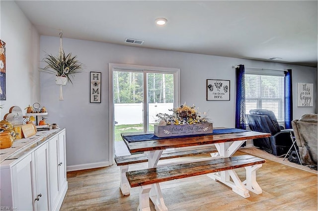 dining room featuring light wood-type flooring, a healthy amount of sunlight, visible vents, and baseboards