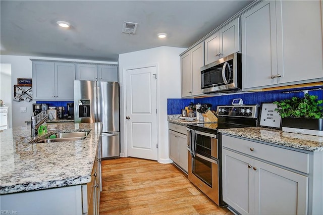 kitchen with appliances with stainless steel finishes, decorative backsplash, sink, light wood-type flooring, and light stone countertops