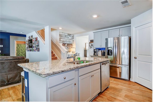 kitchen featuring light hardwood / wood-style flooring, a center island with sink, light stone counters, and stainless steel appliances