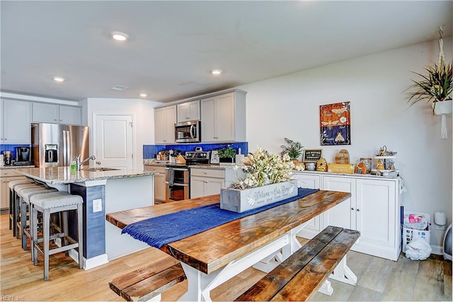 kitchen featuring tasteful backsplash, light wood-type flooring, light stone countertops, and stainless steel appliances