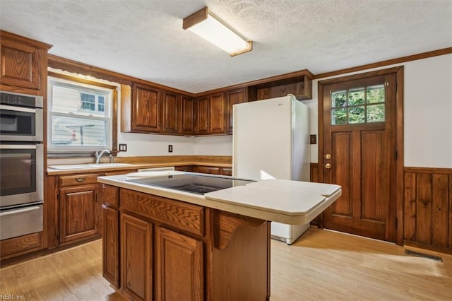 kitchen featuring light wood-type flooring, stainless steel double oven, black electric cooktop, a textured ceiling, and a center island