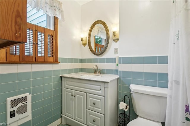 bathroom with heating unit, toilet, vanity, and tile walls