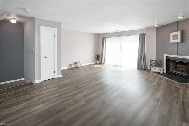 unfurnished living room with a fireplace with raised hearth, wood finished floors, and baseboards