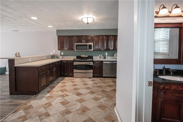 kitchen with stainless steel appliances, a peninsula, a sink, dark brown cabinets, and light countertops