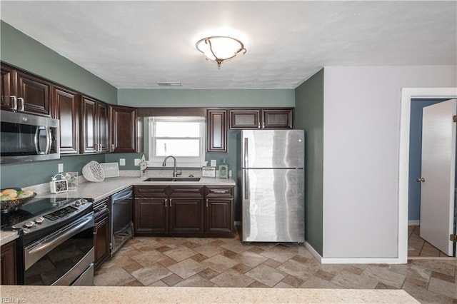 kitchen with appliances with stainless steel finishes, light countertops, a sink, and dark brown cabinetry