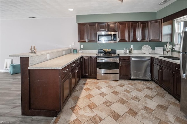 kitchen with a peninsula, appliances with stainless steel finishes, light countertops, and dark brown cabinets