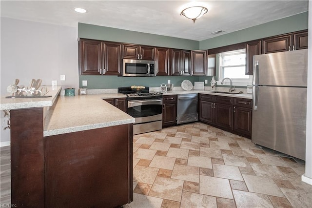 kitchen featuring stainless steel appliances, a peninsula, a sink, and light countertops