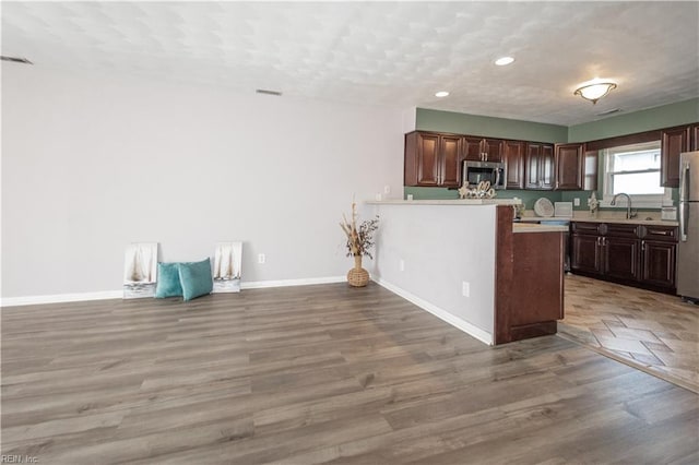 kitchen featuring light countertops, light wood-style flooring, appliances with stainless steel finishes, a sink, and baseboards