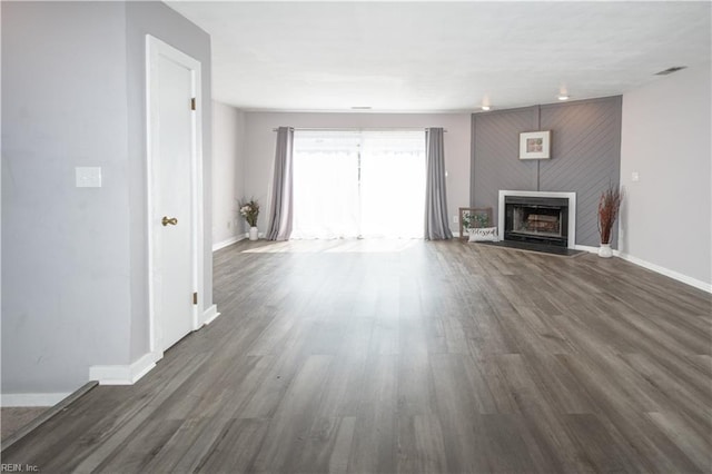 unfurnished living room featuring visible vents, baseboards, a fireplace with raised hearth, and wood finished floors