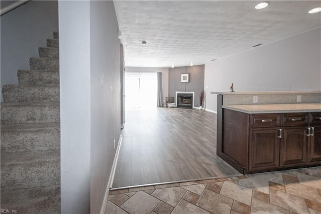 kitchen with dark brown cabinetry, baseboards, open floor plan, a fireplace, and recessed lighting