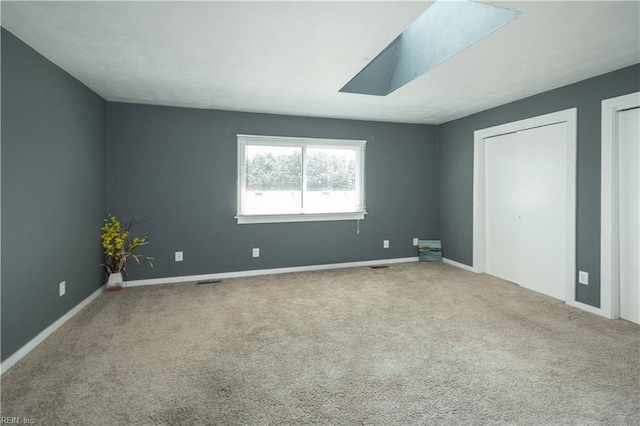 unfurnished bedroom with carpet floors, a skylight, baseboards, and multiple closets