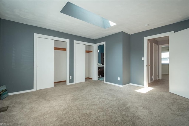 unfurnished bedroom with multiple closets, a skylight, carpet flooring, and baseboards