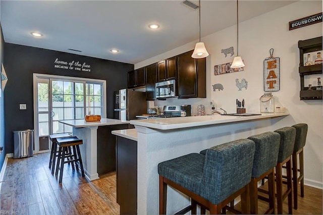 kitchen featuring visible vents, appliances with stainless steel finishes, a kitchen breakfast bar, wood finished floors, and light countertops