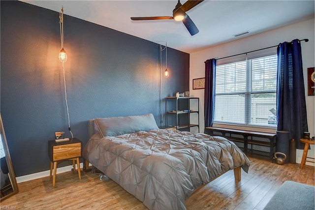 bedroom featuring a ceiling fan, baseboards, visible vents, and wood finished floors